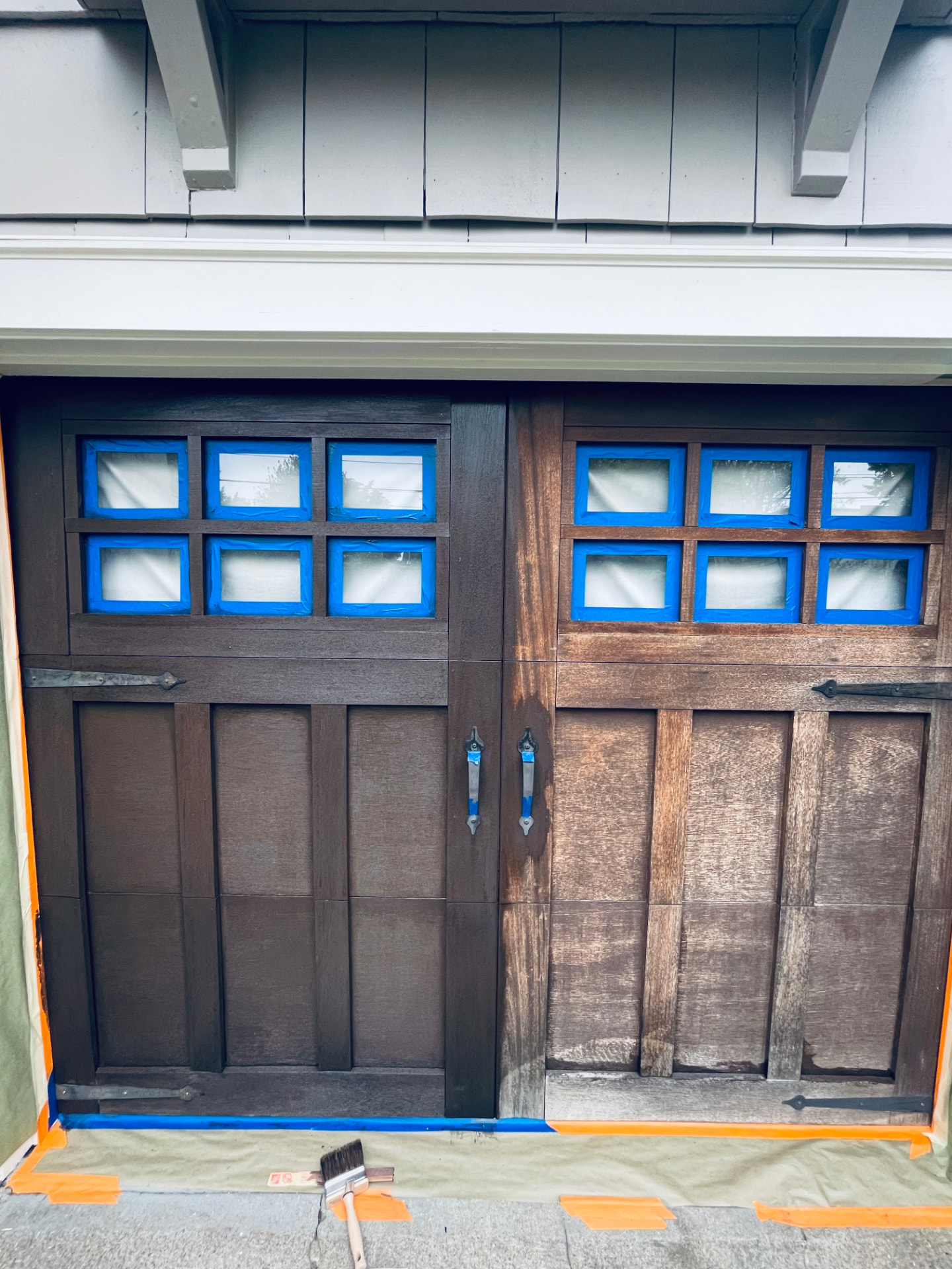 Wooden garage door mid-stain showing contrast between old light wood and new dark stain.