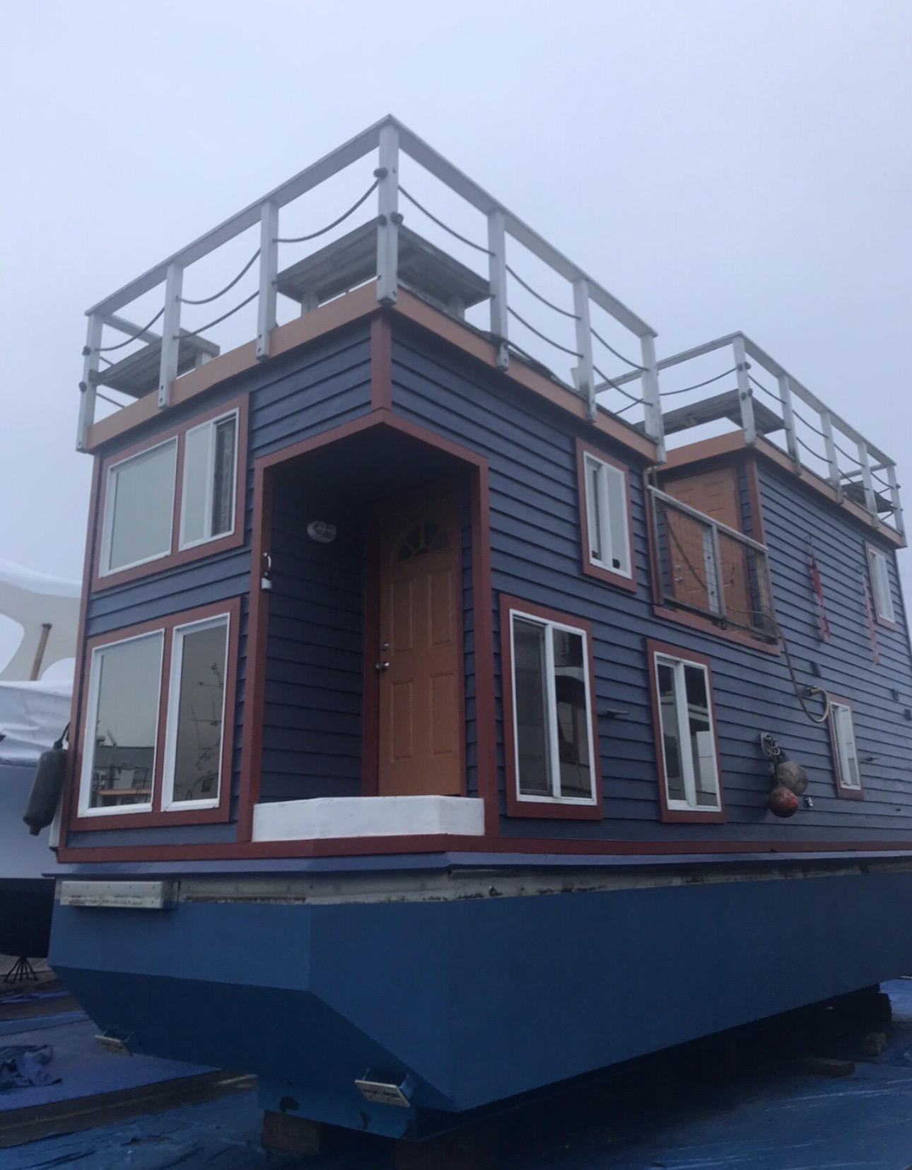 Same houseboat finished with deep navy siding and dark red-brown trim.