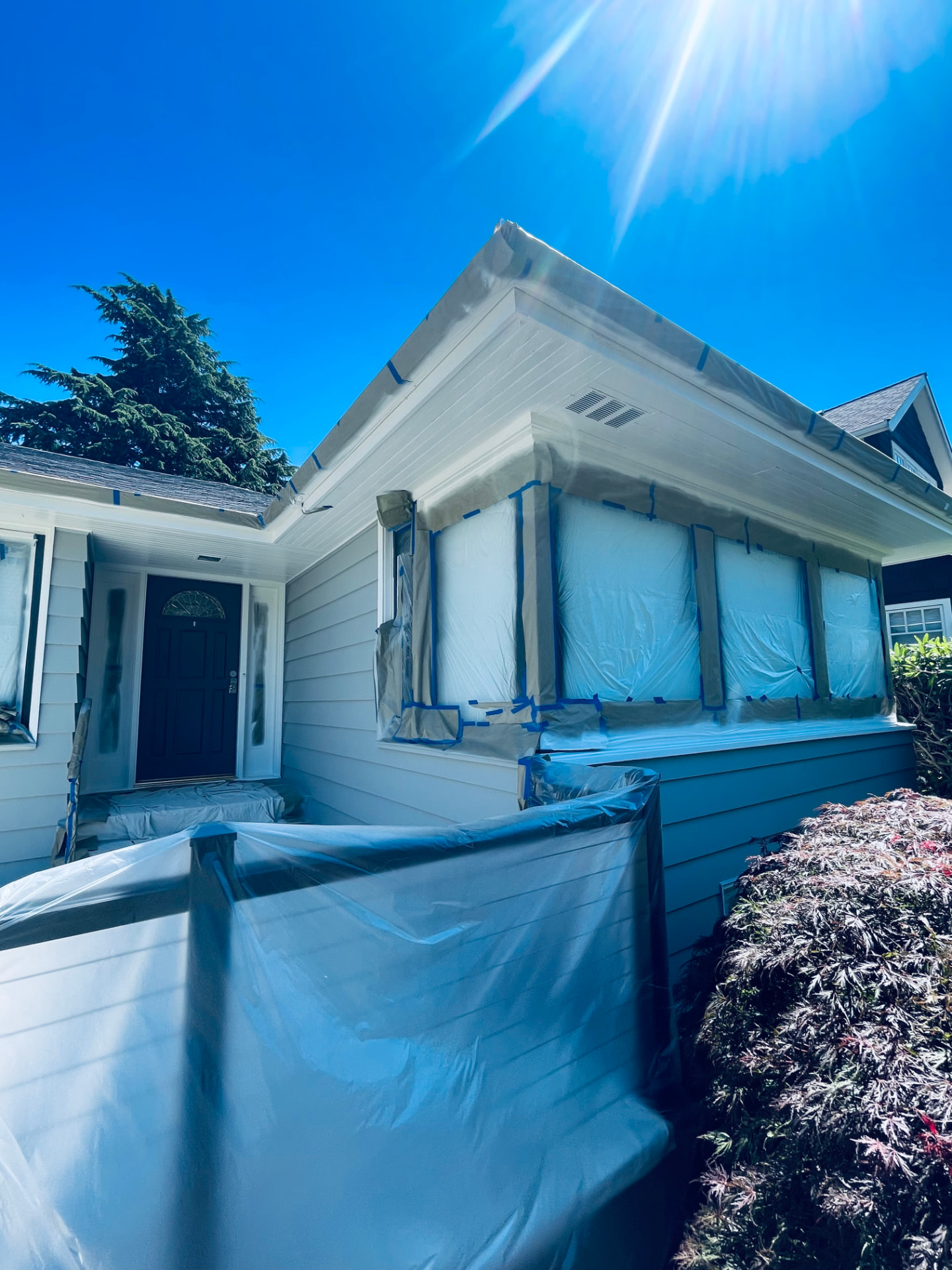 Single-story gray house covered in plastic sheeting during exterior prep.