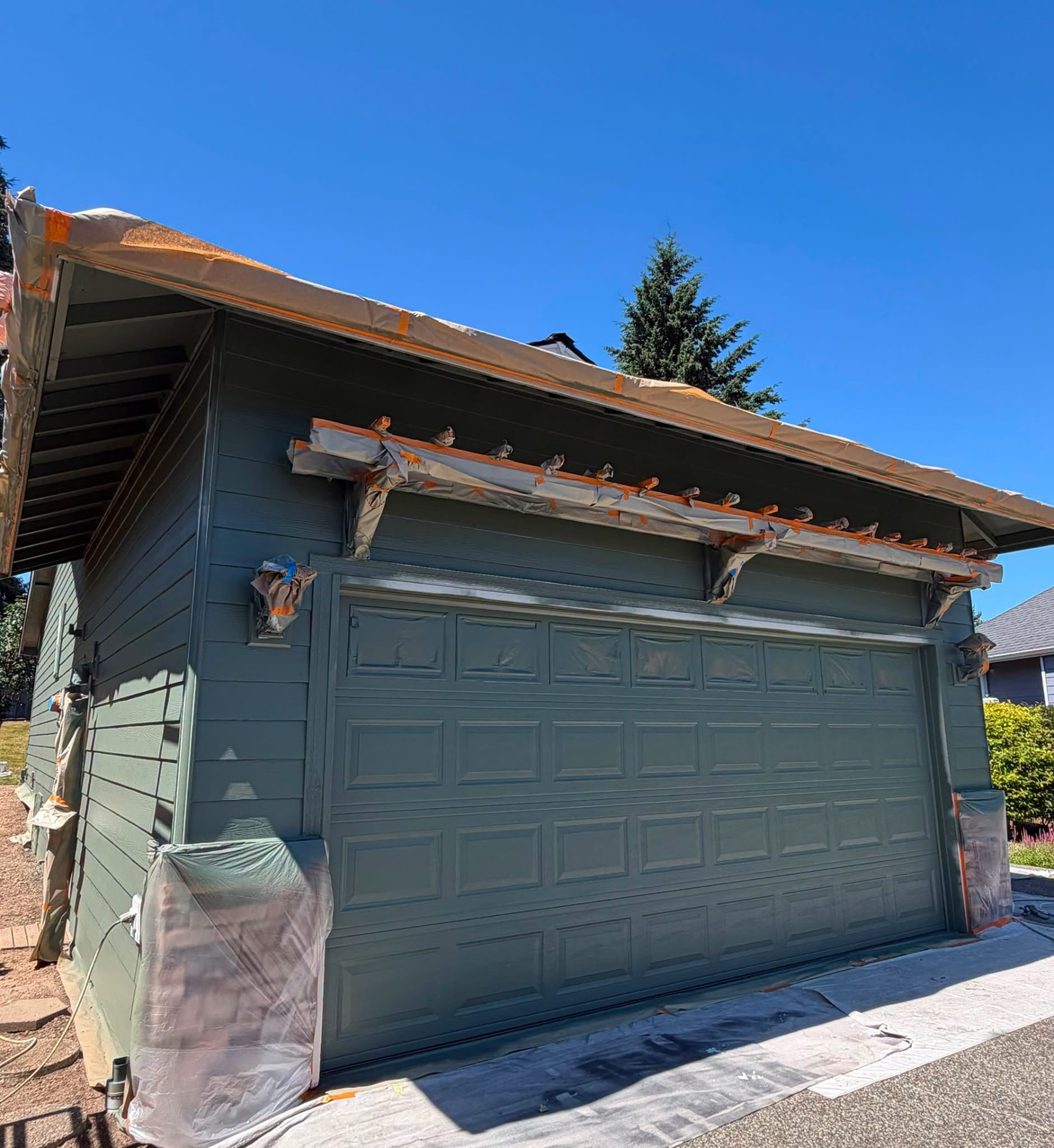 Garage mid-painting with plastic and tape protecting the driveway.