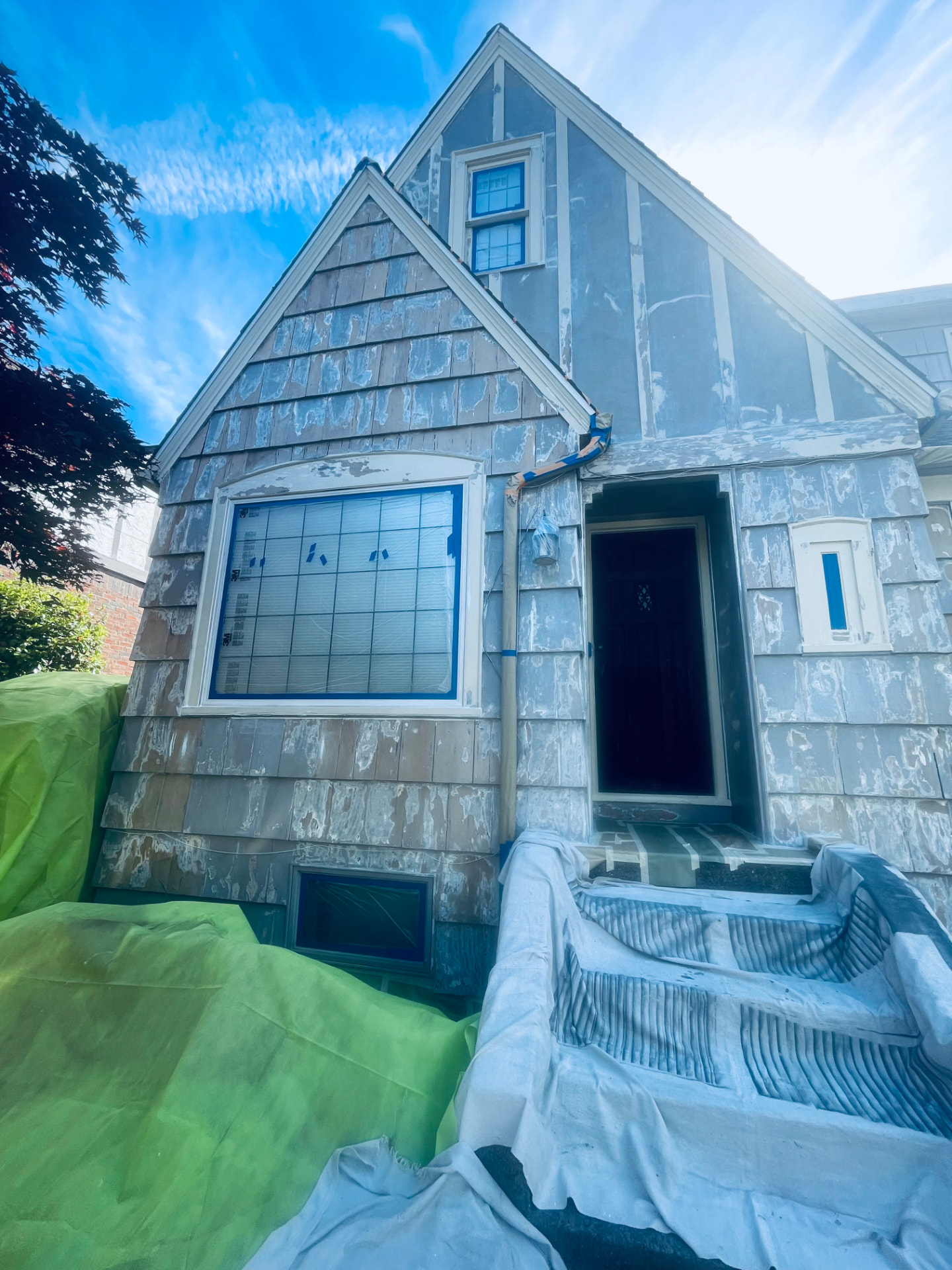 Two-story Tudor-style house during prep with siding stripped and windows masked.