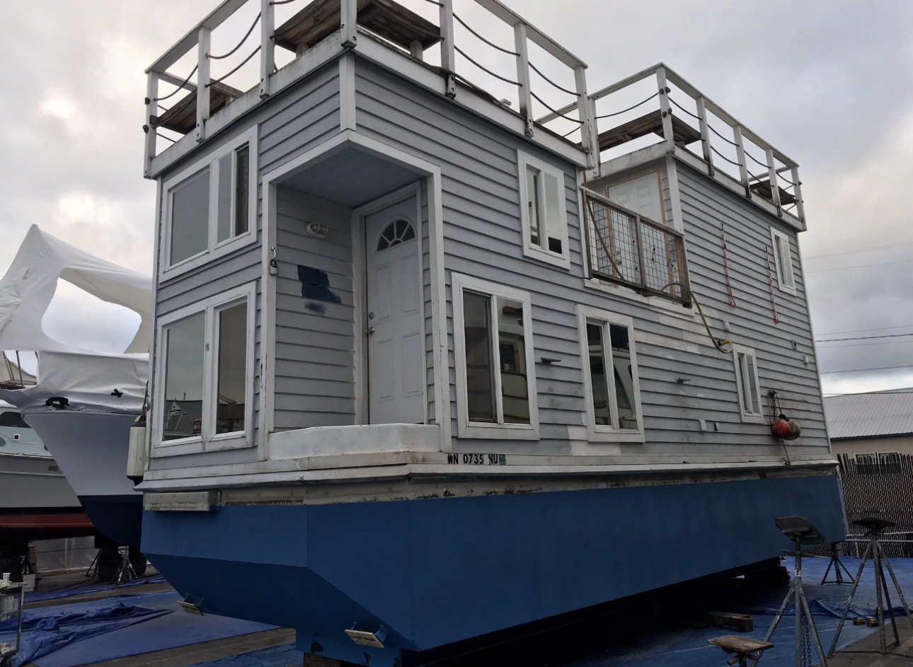 Large gray houseboat with white trim and multiple decks before repaint.